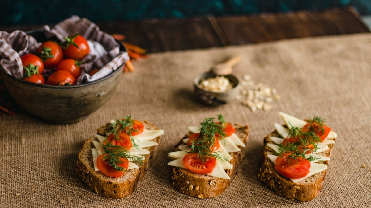 Rustic multigrain bread topped with cheese, tomatoes, and dill on a burlap surface, perfect for food photography.